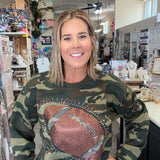 A woman wearing a camouflage crewneck sweatshirt with a large brown football graphic on the front, standing inside a retail shop.