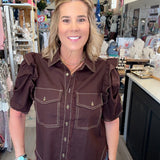 A woman wearing a dark brown western-style puff-sleeve shirt with contrast stitching and blue jeans, standing inside a retail store.