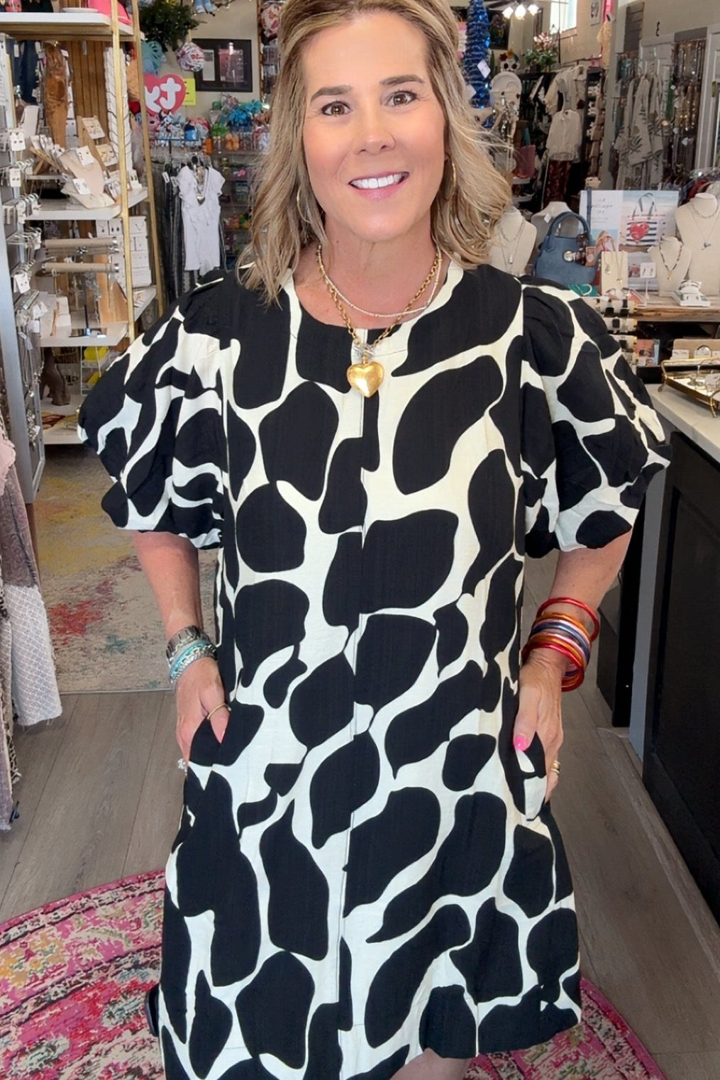 A woman modeling a short puff-sleeve dress with a bold black and white organic spot pattern, standing inside a boutique shop.
