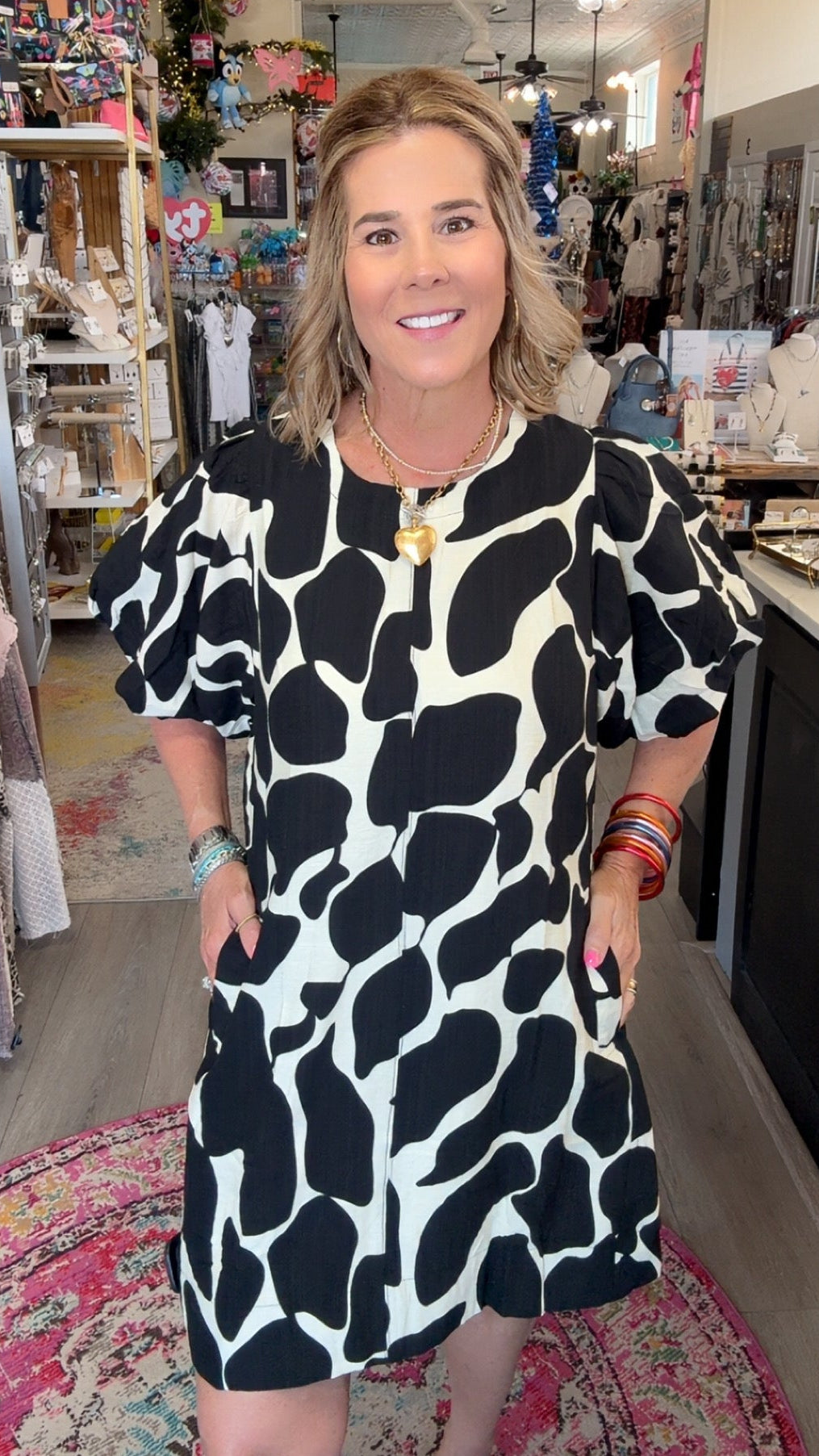 A woman modeling a short puff-sleeve dress with a bold black and white organic spot pattern, standing inside a boutique shop.