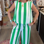 A woman modeling a sleeveless green and white vertically striped jumpsuit inside a retail boutique.