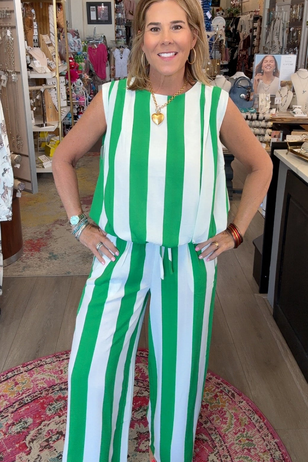A woman modeling a sleeveless green and white vertically striped jumpsuit inside a retail boutique.