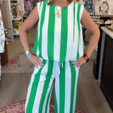 A woman modeling a sleeveless green and white vertically striped jumpsuit inside a retail boutique.