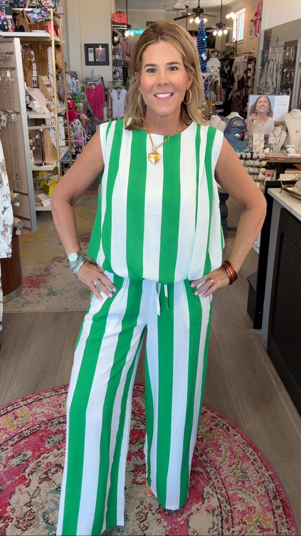 A woman modeling a sleeveless green and white vertically striped jumpsuit inside a retail boutique.