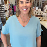 A woman wearing a light blue short-sleeve V-neck top and blue jeans, standing in a retail store environment.