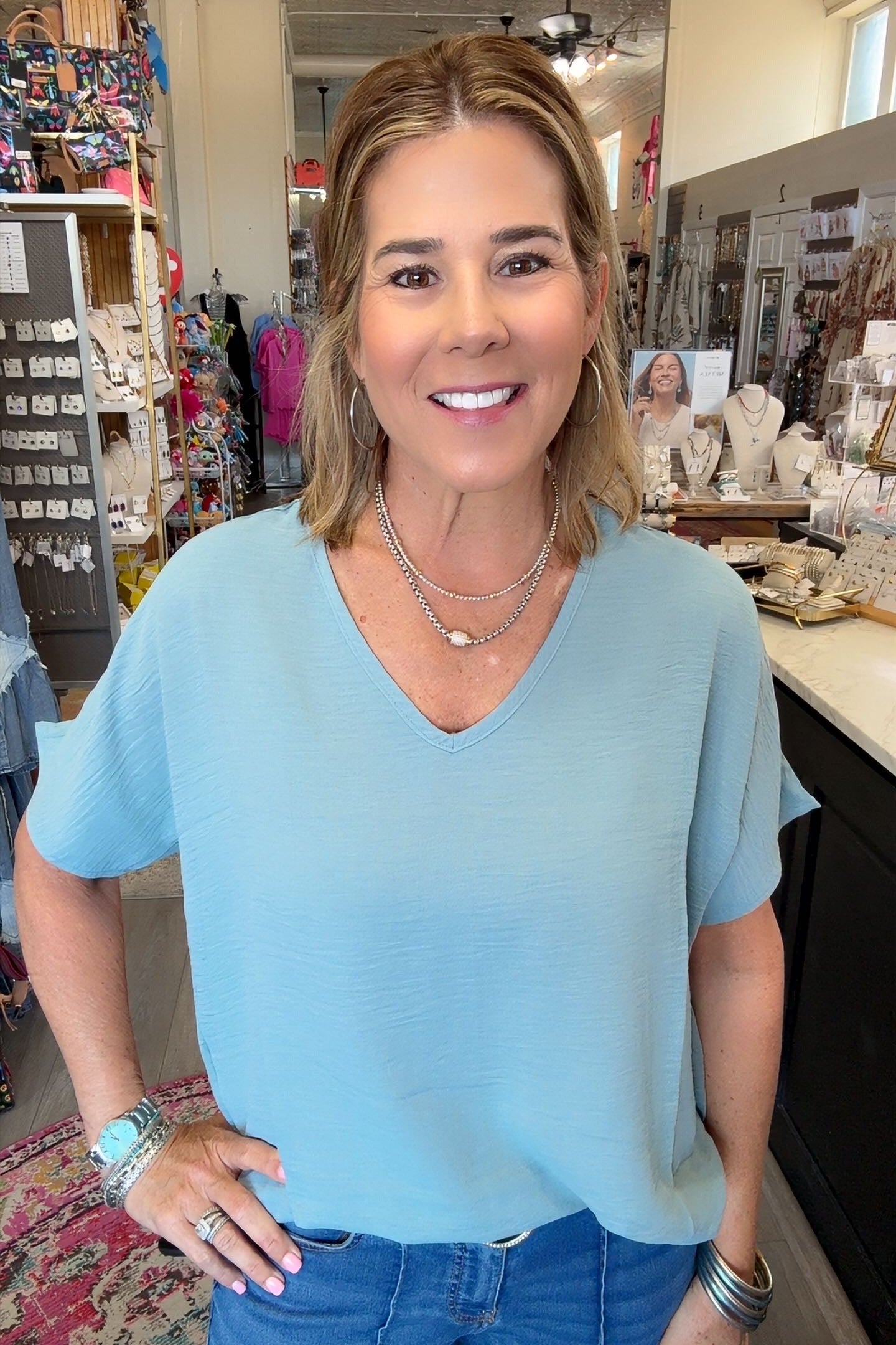 A woman wearing a light blue short-sleeve V-neck top and blue jeans, standing in a retail store environment.