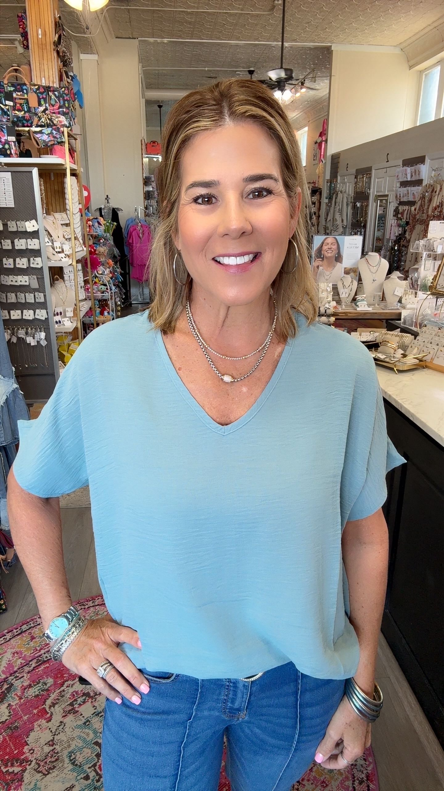 A woman wearing a light blue short-sleeve V-neck top and blue jeans, standing in a retail store environment.