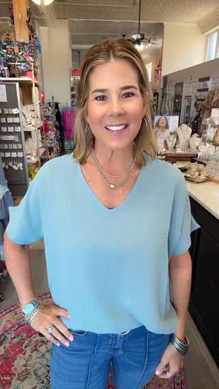 A woman wearing a light blue short-sleeve V-neck top and blue jeans, standing in a retail store environment.