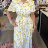 A woman modeling a white short-sleeve midi dress with a yellow abstract pattern, standing inside a retail boutique.