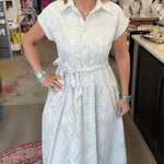 A woman wearing a white short-sleeve dress with a subtle textured pattern, standing in a retail store interior.