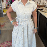 A woman wearing a white short-sleeve dress with a subtle textured pattern, standing in a retail store interior.