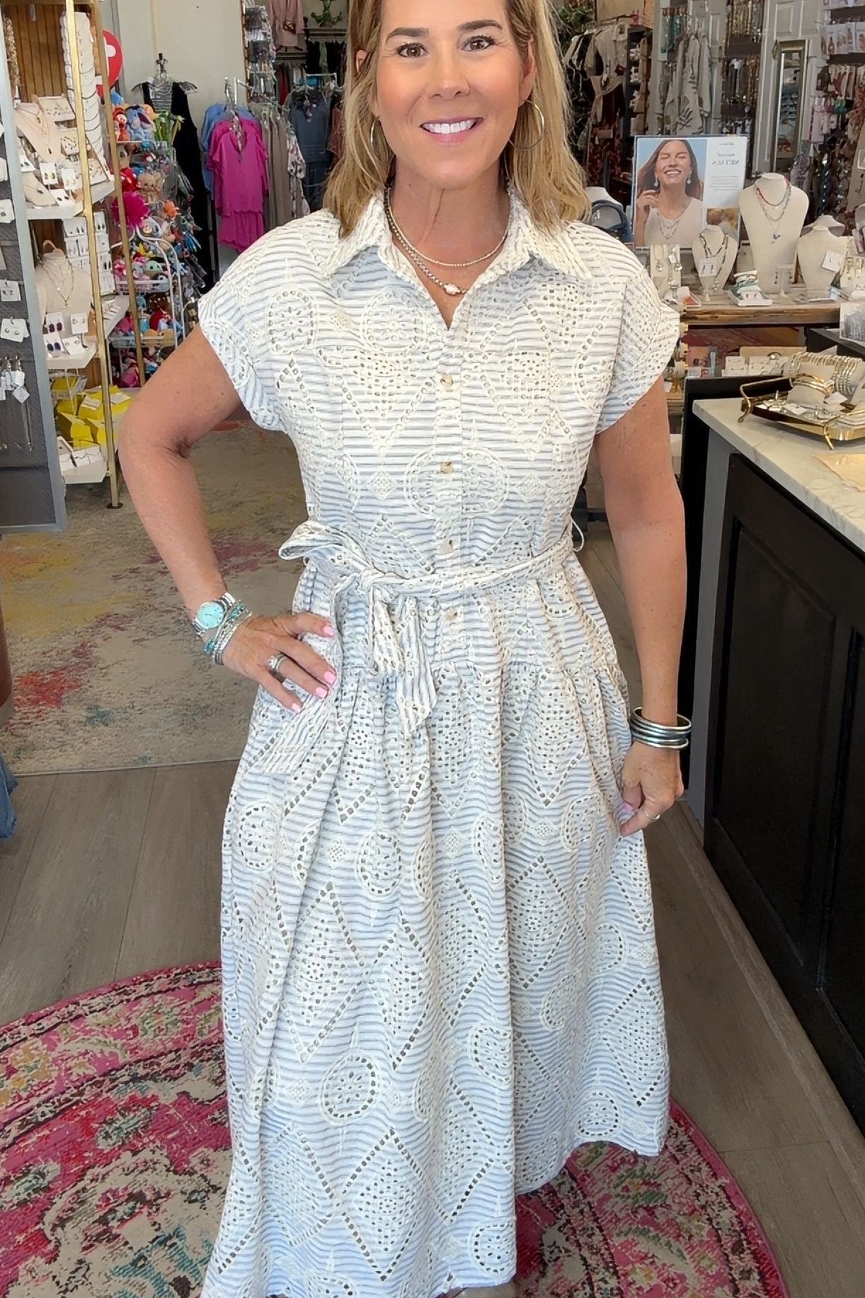 A woman wearing a white short-sleeve dress with a subtle textured pattern, standing in a retail store interior.