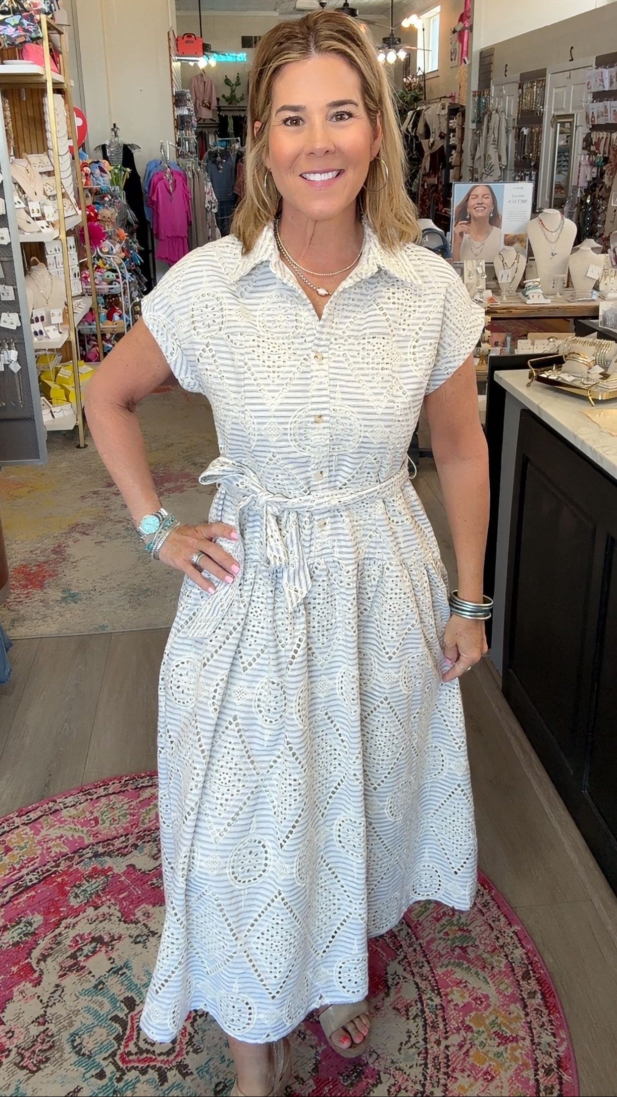 A woman wearing a white short-sleeve dress with a subtle textured pattern, standing in a retail store interior.