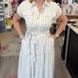 A woman modeling a white and light blue vertically striped shirt dress inside a boutique store.