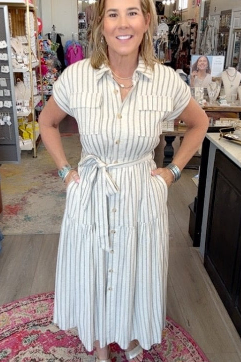 A woman modeling a white and light blue vertically striped shirt dress inside a boutique store.