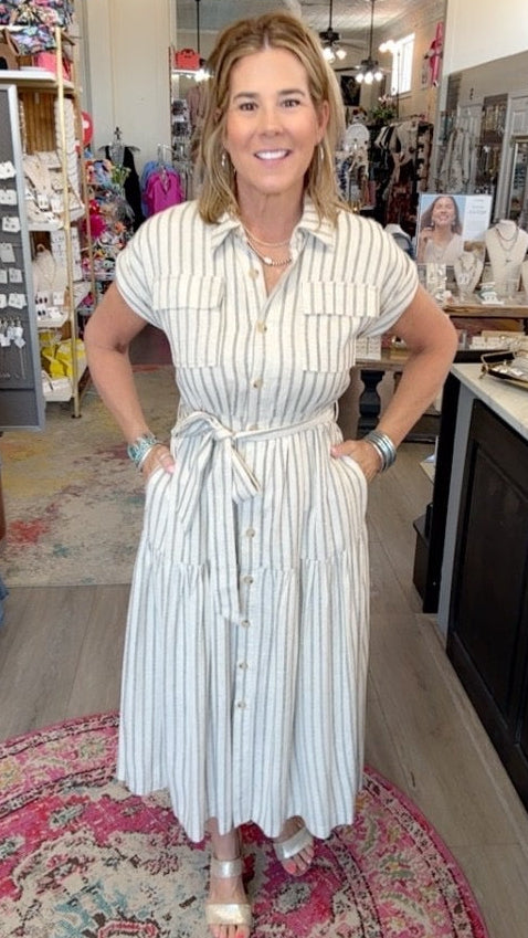 A woman modeling a white and light blue vertically striped shirt dress inside a boutique store.