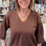 A woman with blonde hair wearing a brown short-sleeve V-neck top and blue jeans, standing in a retail store.