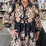 A woman modeling a black button-up dress with beige and pink floral patterns, standing inside a retail boutique.