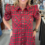 A woman modeling a red and green plaid puff-sleeve shirt dress inside a boutique store.