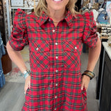 A woman modeling a red and green plaid puff-sleeve shirt dress inside a boutique store.