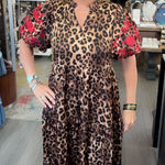 A woman modeling a leopard print midi dress with red floral puff sleeves in a boutique store.