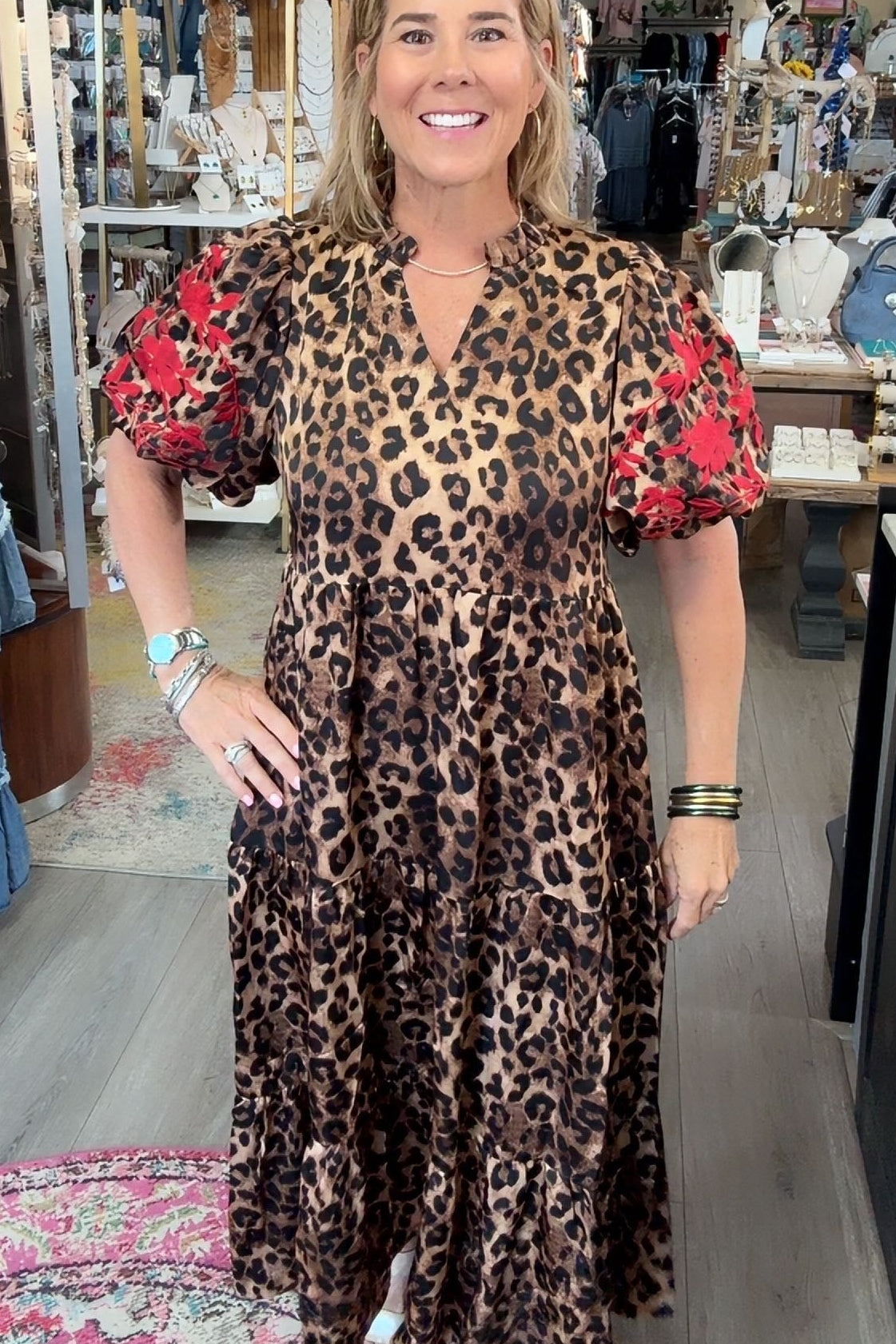 A woman modeling a leopard print midi dress with red floral puff sleeves in a boutique store.