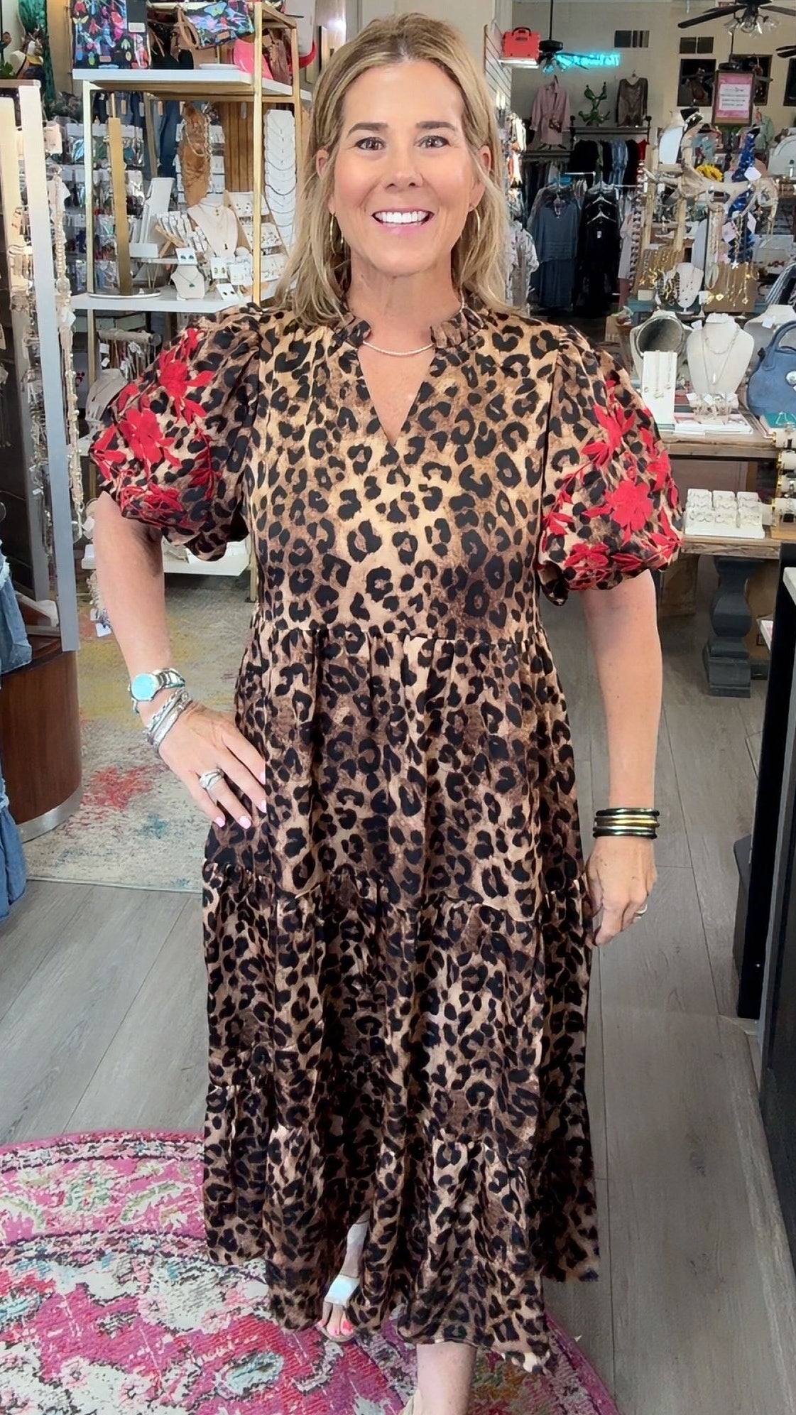 A woman modeling a leopard print midi dress with red floral puff sleeves in a boutique store.