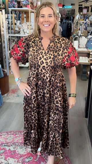 A woman modeling a leopard print midi dress with red floral puff sleeves in a boutique store.
