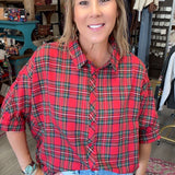 A woman wearing a red and green plaid short-sleeve button-up shirt with light blue jeans, standing in a retail store.