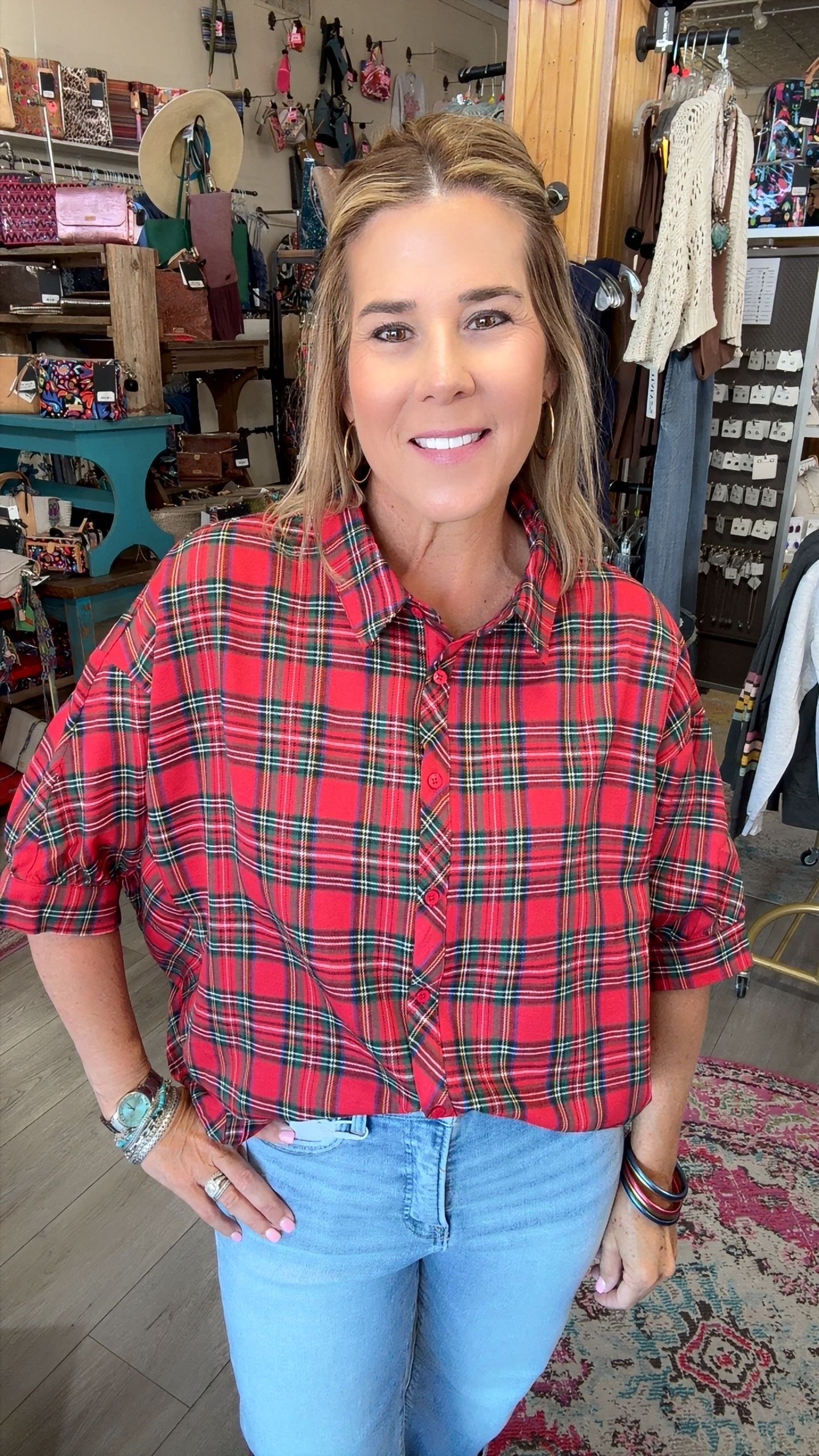 A woman wearing a red and green plaid short-sleeve button-up shirt with light blue jeans, standing in a retail store.