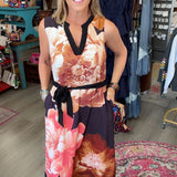A woman modeling a sleeveless V-neck dress with a large floral print in pink, orange, and dark navy, standing inside a boutique shop.