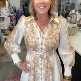 A woman modeling a long-sleeve button-front dress with a beige and white toile pattern, standing inside a retail store.
