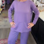 A woman modeling a matching lavender lounge set consisting of a long-sleeve top and wide-leg pants, standing in a retail store.