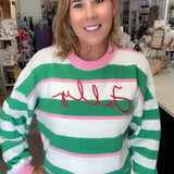 A woman wearing a green, white, and pink striped sweater with 'Folly' embroidered in red across the chest, standing in a retail store.