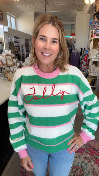 A woman wearing a green, white, and pink striped sweater with 'Folly' embroidered in red across the chest, standing in a retail store.