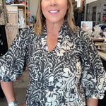 A woman wearing a black and white damask-patterned blouse with puff sleeves, styled with blue jeans and a brown leather belt with a large silver buckle, standing in a retail store.