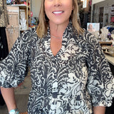 A woman wearing a black and white damask-patterned blouse with puff sleeves, styled with blue jeans and a brown leather belt with a large silver buckle, standing in a retail store.