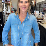 A woman wearing a light blue denim button-up shirt with silver rhinestone embellishments, standing in a retail store.