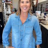 A woman wearing a light blue denim button-up shirt with silver rhinestone embellishments, standing in a retail store.