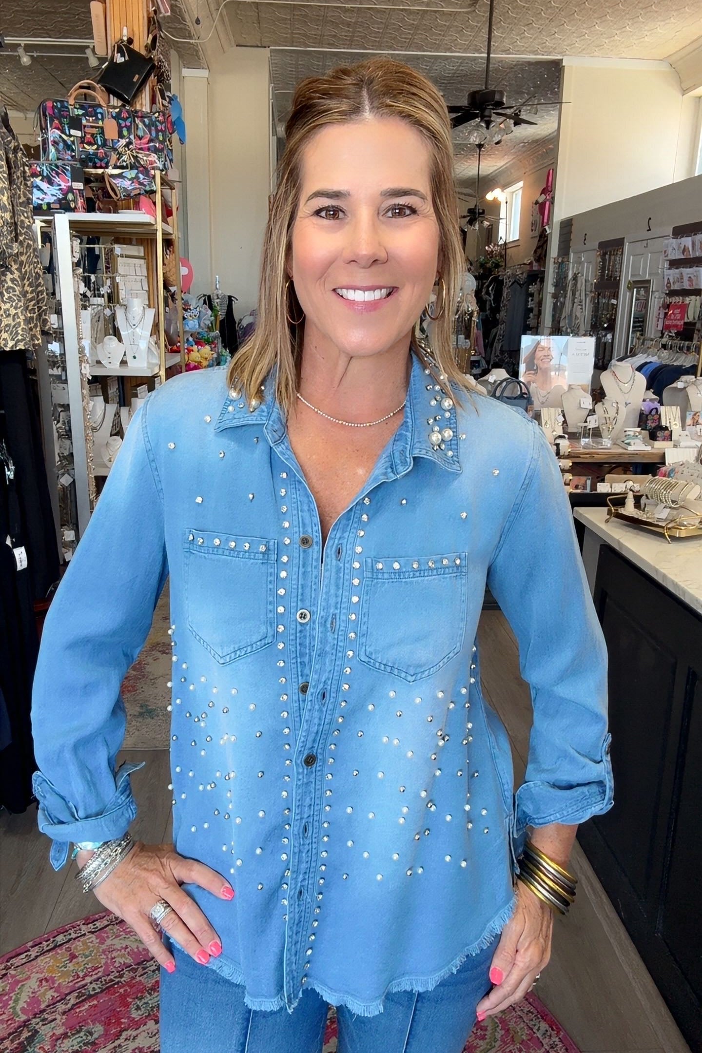 A woman wearing a light blue denim button-up shirt with silver rhinestone embellishments, standing in a retail store.
