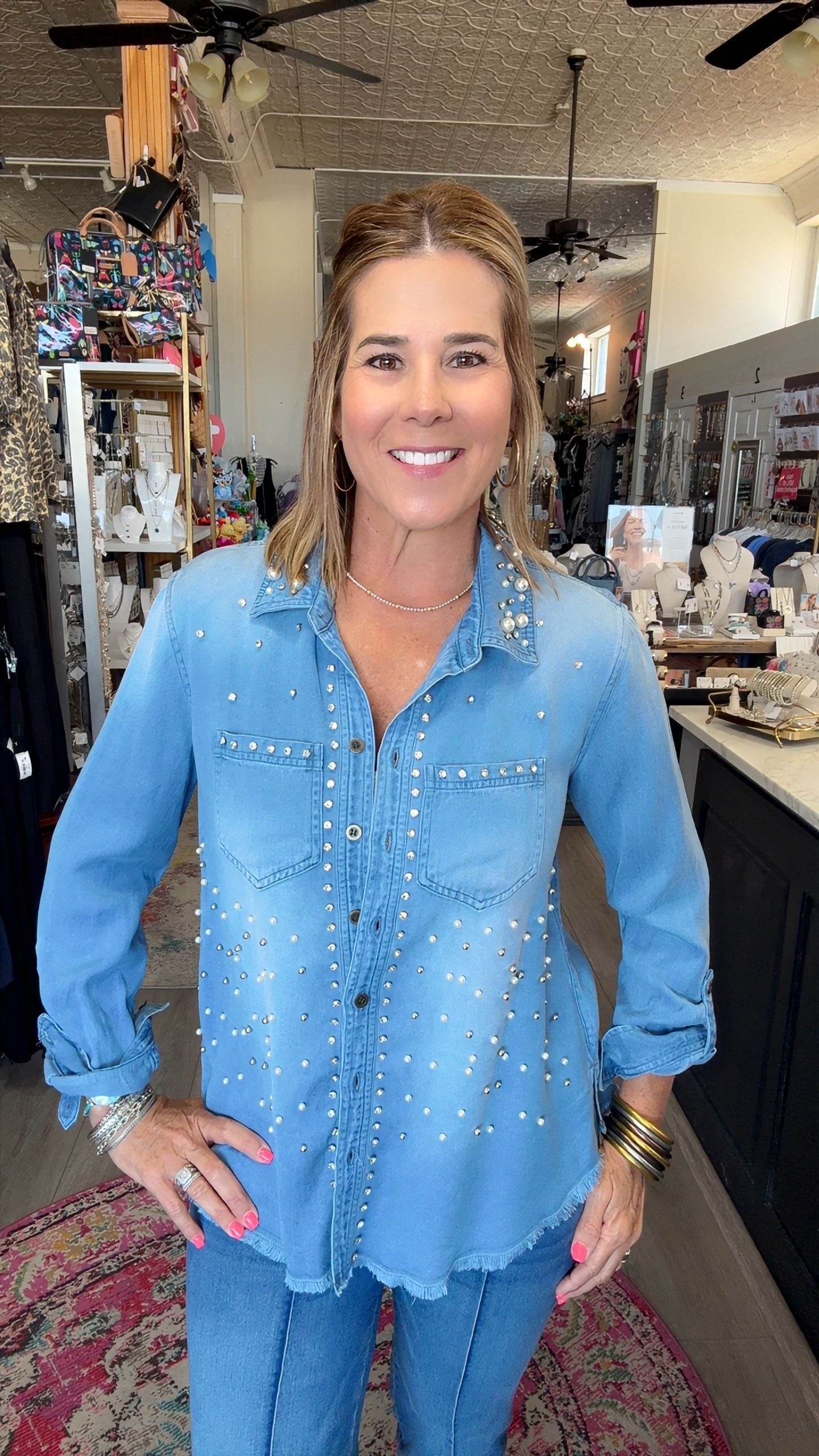 A woman wearing a light blue denim button-up shirt with silver rhinestone embellishments, standing in a retail store.