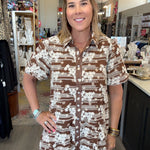 A woman wearing a brown and white patterned short-sleeve button-up shirt dress, standing inside a retail store.