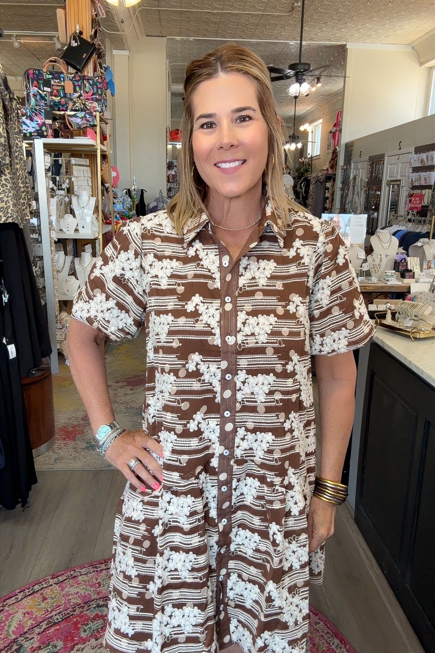 A woman wearing a brown and white patterned short-sleeve button-up shirt dress, standing inside a retail store.