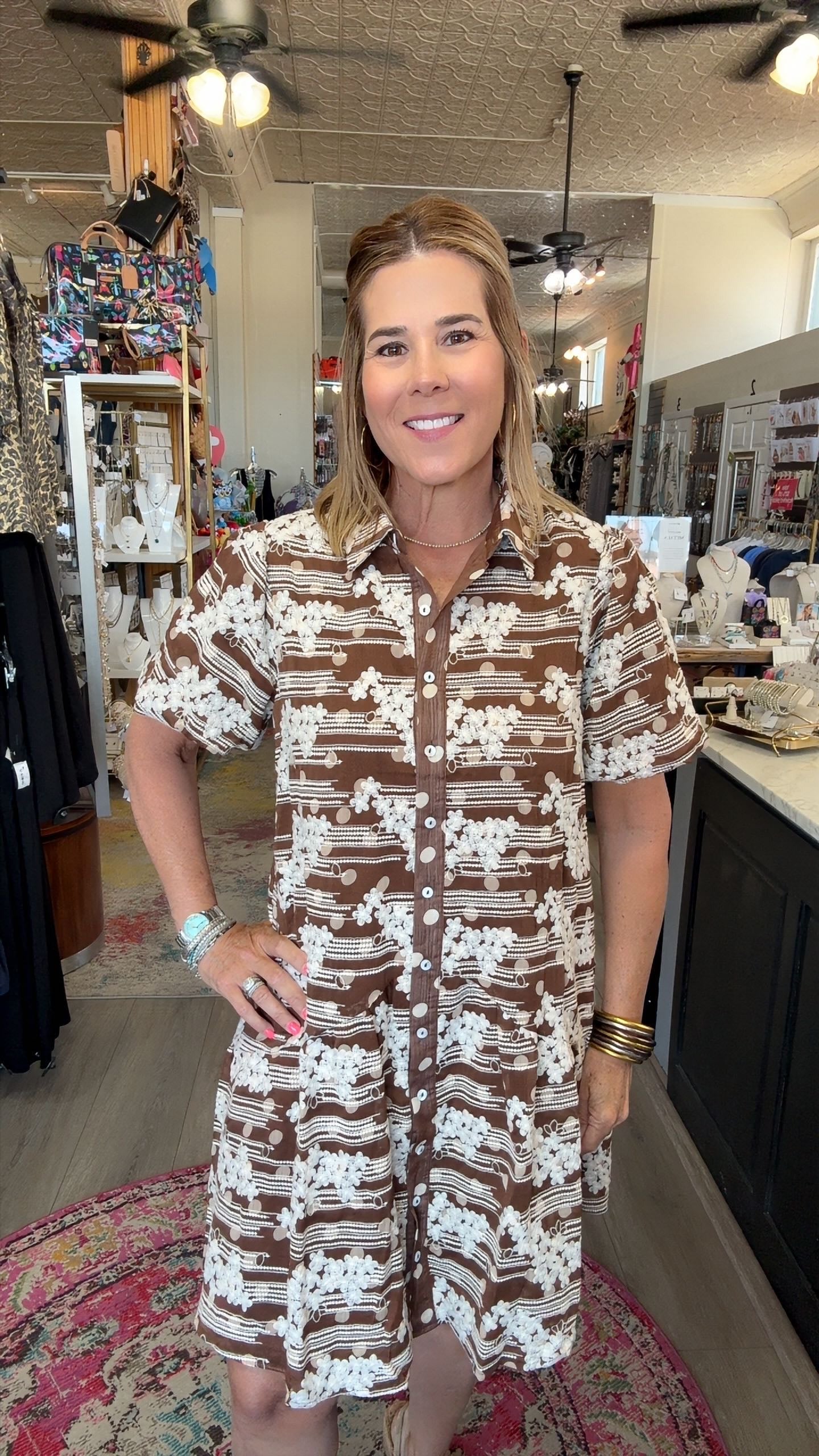 A woman wearing a brown and white patterned short-sleeve button-up shirt dress, standing inside a retail store.