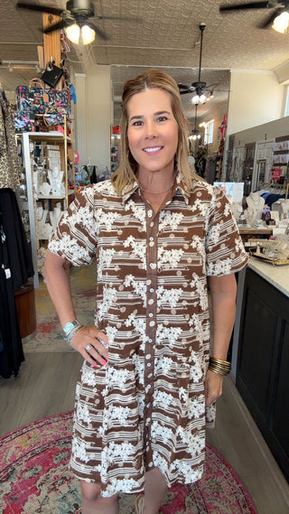 A woman wearing a brown and white patterned short-sleeve button-up shirt dress, standing inside a retail store.