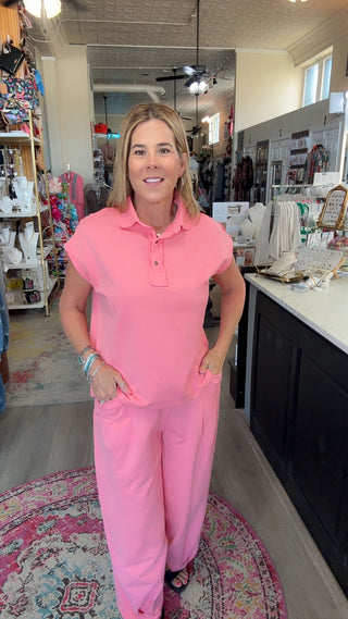 A woman modeling a bright pink short-sleeve polo shirt and matching wide-leg pants in a retail store setting.