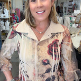 A woman with blonde hair stands in a retail store wearing a beige fringed blouse with a vintage-style floral print featuring red roses and black leaves.