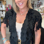A woman wearing a black feathered fringe vest over a cream top and khaki pants, standing in a retail store interior.