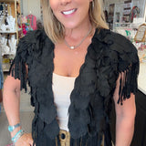 A woman wearing a black feathered fringe vest over a cream top and khaki pants, standing in a retail store interior.