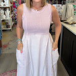 A woman wearing a sleeveless two-tone dress with a light pink bodice and a white skirt with side pockets, standing inside a retail boutique.